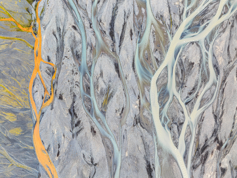 Aerial view of a complex braided river system with vibrant blue glacial meltwater and striking orange mineral deposits flowing through dark volcanic sediment in Iceland. Aerial view of a complex braided river system with vibrant blue glacial meltwater and striking orange mineral deposits flowing through dark volcanic sediment in Iceland.