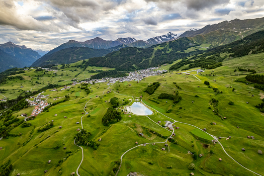 Aerial view of the village of Prutz nestled in the green alpine landscape of Tyrol featuring meadows a mountain lake and distant peaks under a cloudy sky in Prutz Tyrol Austria. Aerial view of the village of Prutz nestled in the green alpine landscape of Tyrol featuring meadows a mountain lake and distant peaks under a cloudy sky in Prutz Tyrol Austria.