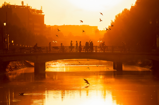 View of people walking and cycling across a bridge over the Dambovita River during a golden sunset in Bucharest Bucharest Romania. View of people walking and cycling across a bridge over the Dambovita River during a golden sunset in Bucharest Bucharest Romania.