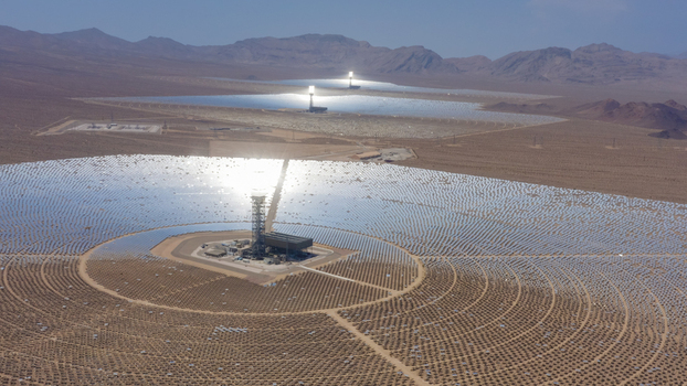 Aerial view of a large concentrated solar power plant with thousands of mirrors and central solar towers in a desert landscape United States.
