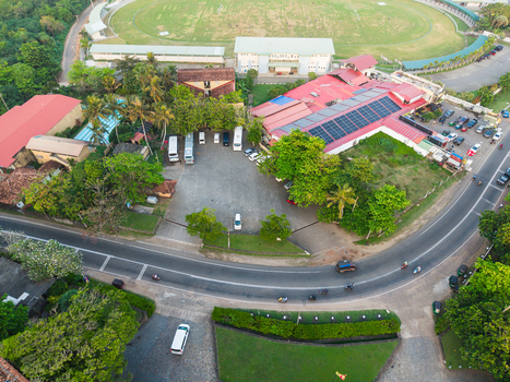 Aerial view of a building complex with solar panels and a parking lot next to a curved road and the Galle International Stadium in Galle Southern Province Sri Lanka. Aerial view of a building complex with solar panels and a parking lot next to a curved road and the Galle International Stadium in Galle Southern Province Sri Lanka.