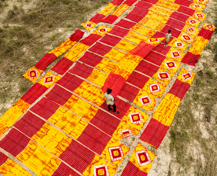 Narayanganj Bangladesh 30 March 2026 Aerial view of vibrant red and yellow textiles drying under the sun creating a striking geometric pattern on the sandy ground.
