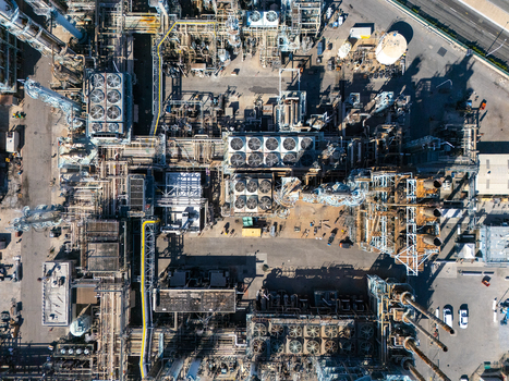 Aerial view of an industrial oil refinery complex featuring complex piping networks cooling towers storage tanks and metallic structures in Carson California United States.