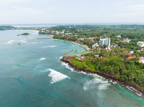 Aerial view of Coconut Tree Hill with turquoise ocean waves crashing against the rocky shore and lush tropical palm trees in Mirissa Southern Province Sri Lanka. Aerial view of Coconut Tree Hill with turquoise ocean waves crashing against the rocky shore and lush tropical palm trees in Mirissa Southern Province Sri Lanka.