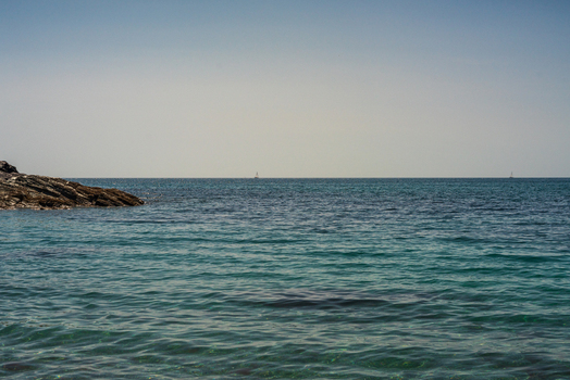 View of Lansallos beach with calm turquoise waters a rocky outcrop on the left and a clear horizon under a bright sky in Lansallos England United Kingdom. View of Lansallos beach with calm turquoise waters a rocky outcrop on the left and a clear horizon under a bright sky in Lansallos England United Kingdom.