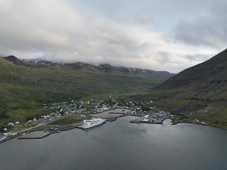 Aerial view of Seydisfjordur town nestled in a deep fjord with a cruise ship docked at the harbor surrounded by dramatic mountains and green slopes in Seydisfjordur Mulathing Iceland.