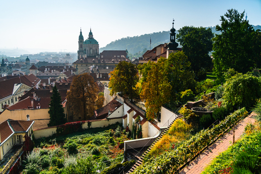 View of the historic rooftops and the dome of St. Nicholas Church in the Lesser Town with lush gardens and trees in the foreground in Prague Prague Czechia.