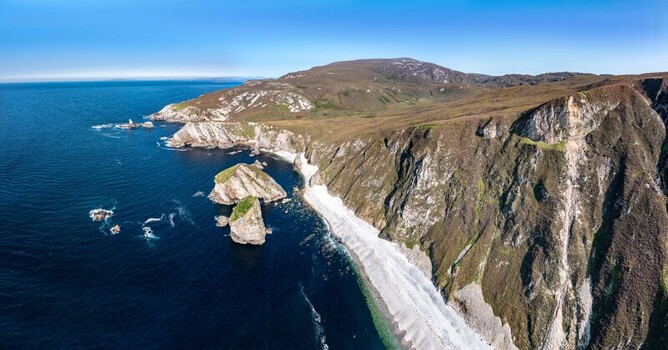 Aerial view of the dramatic cliffs and rugged coastline of Glenlough Bay with deep blue sea and a secluded beach in Ardara County Donegal Ireland.