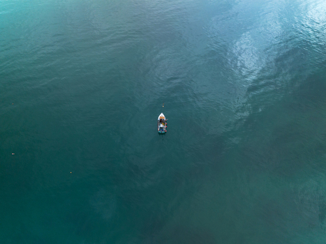 Aerial view of a small boat floating on the calm deep blue green sea in Looe Cornwall United Kingdom. Aerial view of a small boat floating on the calm deep blue green sea in Looe Cornwall United Kingdom.