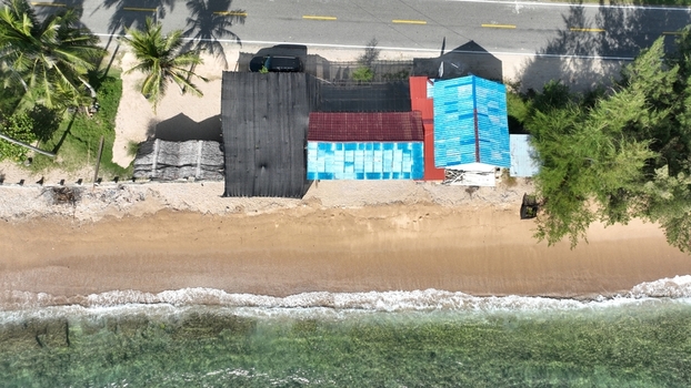 Aerial view of a small coastal building with a blue roof situated next to a road and a sandy beach in Tapak Tuan Aceh Indonesia. Aerial view of a small coastal building with a blue roof situated next to a road and a sandy beach in Tapak Tuan Aceh Indonesia.