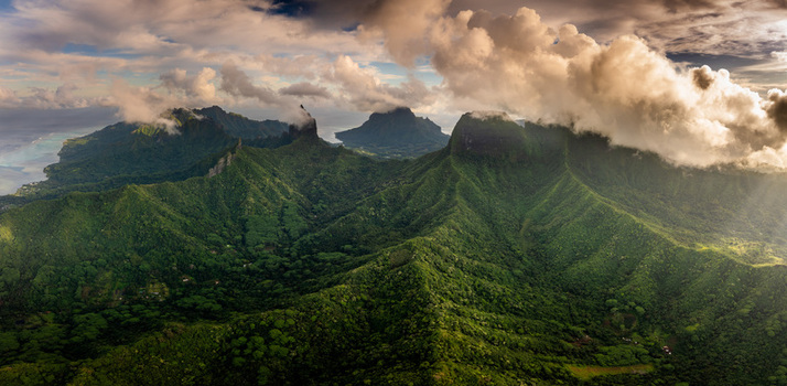 Aerial view of the lush volcanic peaks and dense tropical forests under dramatic clouds at sunset Moorea Maiao Windward Islands French Polynesia. Aerial view of the lush volcanic peaks and dense tropical forests under dramatic clouds at sunset Moorea Maiao Windward Islands French Polynesia.
