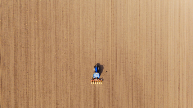 Aerial view of a lone tractor tilling the ochre earth creating rhythmic furrows in the vast field Sremska Mitrovica Vojvodina Serbia. Aerial view of a lone tractor tilling the ochre earth creating rhythmic furrows in the vast field Sremska Mitrovica Vojvodina Serbia.