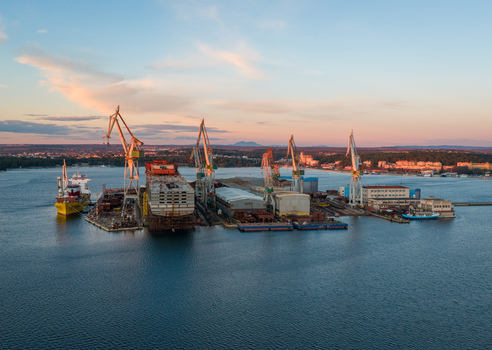 Aerial view of Uljanik Shipyard with industrial cranes docked ships and shipyard facilities along the waterfront at sunset in Pula Croatia. Aerial view of Uljanik Shipyard with industrial cranes docked ships and shipyard facilities along the waterfront at sunset in Pula Croatia.