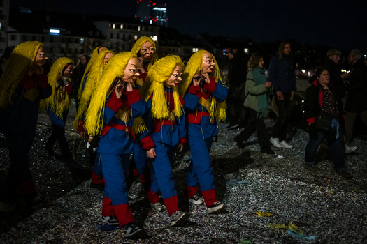 Basel Switzerland 10 March 2025 View of masked figures in vibrant blue and yellow costumes parade through confetti strewn streets during Fasnacht a stark contrast to the dark night. Basel Switzerland 10 March 2025 View of masked figures in vibrant blue and yellow costumes parade through confetti strewn streets during Fasnacht a stark contrast to the dark night.