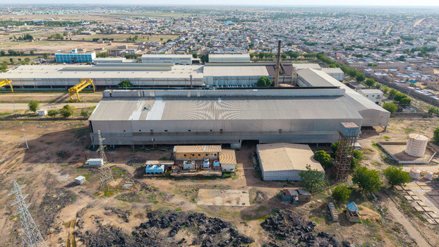 Aerial view of the Katsina Steel Rolling Co. Ltd. industrial facility featuring large metal warehouses a tall chimney and water storage tanks in Katsina Katsina Nigeria.