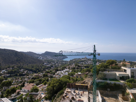 Aerial view of a construction site with a tall crane overlooking the coastal town and Mediterranean Sea in Moraira Valencian Community Spain.