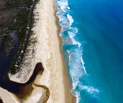 Aerial view of Bettys Beach with turquoise ocean waves sandy shoreline and dark coastal inlet in Albany WA Australia. Aerial view of Bettys Beach with turquoise ocean waves sandy shoreline and dark coastal inlet in Albany WA Australia.