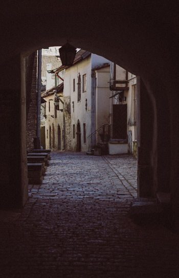 Tallinn Estonia 08 April 2026 View of Vanalinn old town cobblestone street through a dark stone archway with historic buildings and a hanging lantern.