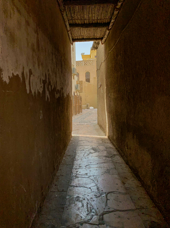 View of a traditional narrow alleyway in Al Fahidi with textured mud walls and stone paved floor under a wooden ceiling in Dubai Dubai United Arab Emirates. View of a traditional narrow alleyway in Al Fahidi with textured mud walls and stone paved floor under a wooden ceiling in Dubai Dubai United Arab Emirates.