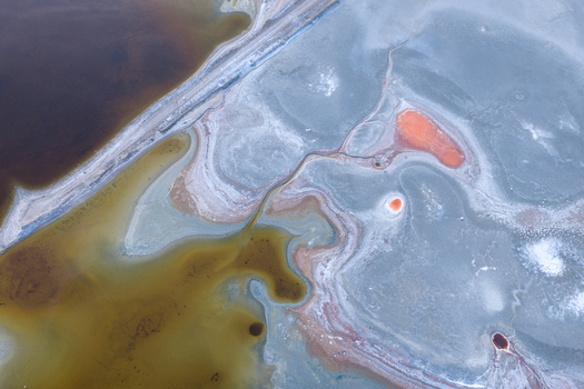 Aerial view of Searles Lake featuring colorful mineral deposits salt crusts and a dirt road crossing the dry lake bed in San Bernardino County California United States. Aerial view of Searles Lake featuring colorful mineral deposits salt crusts and a dirt road crossing the dry lake bed in San Bernardino County California United States.