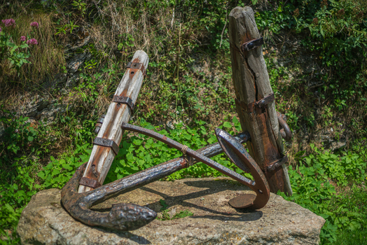 View of an old iron and wooden anchor resting on a stone base in Charlestown Cornwall United Kingdom. View of an old iron and wooden anchor resting on a stone base in Charlestown Cornwall United Kingdom.