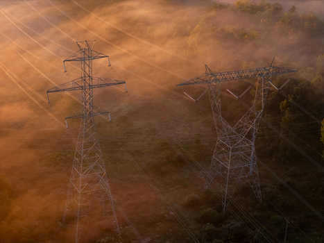 Aerial view of transmission lines and towers rising above a dense layer of morning fog illuminated by the warm light of sunrise in Bridgman Michigan United States.