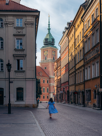 View of a woman in a blue dress walking along a cobblestone street towards the historic Royal Castle clock tower in Warsaw Old Town Warsaw Masovian Voivodeship Poland. View of a woman in a blue dress walking along a cobblestone street towards the historic Royal Castle clock tower in Warsaw Old Town Warsaw Masovian Voivodeship Poland.