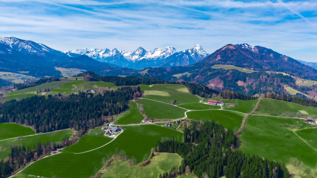 Aerial view of verdant fields nestled amongst rolling hills with patches of dark green forests against a backdrop of snow capped mountains Windischgarsten Upper Austria Austria. Aerial view of verdant fields nestled amongst rolling hills with patches of dark green forests against a backdrop of snow capped mountains Windischgarsten Upper Austria Austria.