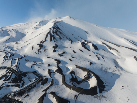 Aerial view of the snow covered southern slope of Mount Etna featuring volcanic craters and dark lava flows under a clear blue sky Nicolosi Sicilia Italy. Aerial view of the snow covered southern slope of Mount Etna featuring volcanic craters and dark lava flows under a clear blue sky Nicolosi Sicilia Italy.