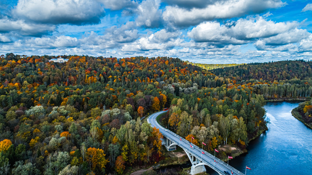 Aerial view of the Gauja River winding through a colorful autumn forest in Sigulda with a bridge crossing the river under a blue sky Sigulda Sigulda Municipality Latvia. Aerial view of the Gauja River winding through a colorful autumn forest in Sigulda with a bridge crossing the river under a blue sky Sigulda Sigulda Municipality Latvia.