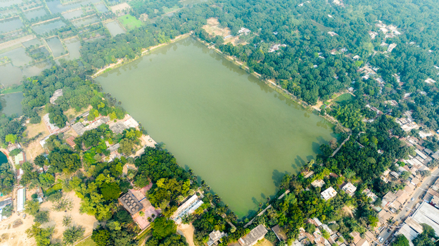 Aerial view of the historic Bagha Shahi Mosque featuring its large rectangular pond surrounded by lush green trees and village architecture in Rajshahi Rajshahi Division Bangladesh.