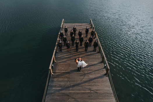 Aerial view of a groom carrying a bride on a wooden pier with uniformed men standing in formation over calm water in Stary Sacz Lesser Poland Voivode Poland.