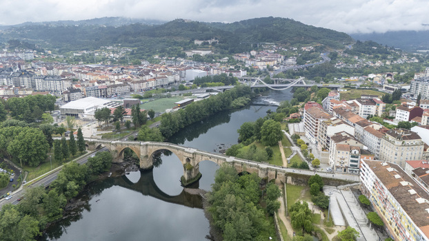 Aerial view of Ponte Vella de Ourense spanning the Minho River with city buildings and green hills under a cloudy sky Ourense Ourense Spain.