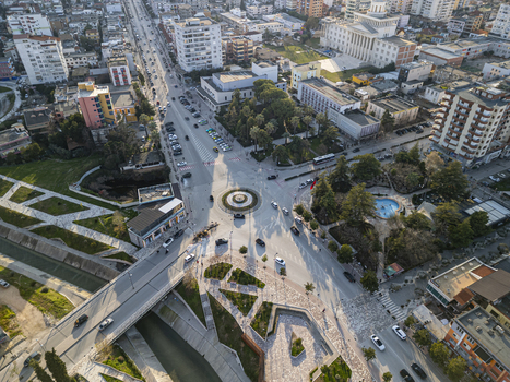 Aerial view of Sheshi Pavaresia with its roundabout surrounding urban buildings a bridge over the Gjanica river and park areas during the golden hour in Fier Qarku i Fierit Albania. Aerial view of Sheshi Pavaresia with its roundabout surrounding urban buildings a bridge over the Gjanica river and park areas during the golden hour in Fier Qarku i Fierit Albania.