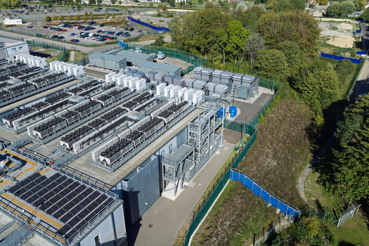 Aerial view of a data center featuring rows of cooling units solar panels on the roof and perimeter fencing in the United Kingdom.