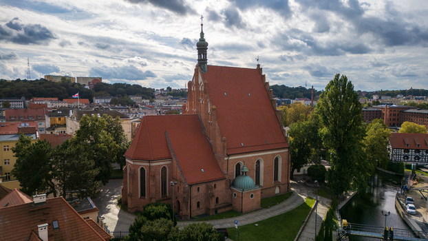 Aerial view of the grand red roofed church standing tall amidst the city s embrace its spire reaching towards the cloudy sky Bydgoszcz Województwo kujawsko pomorskie Poland. Aerial view of the grand red roofed church standing tall amidst the city s embrace its spire reaching towards the cloudy sky Bydgoszcz Województwo kujawsko pomorskie Poland.
