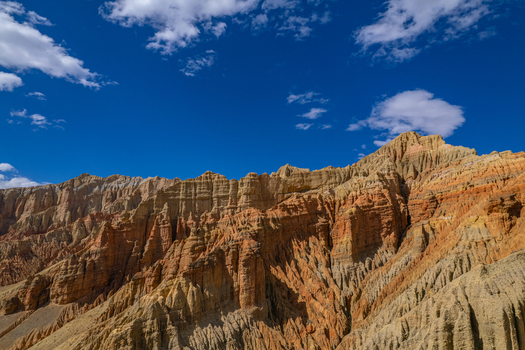 Aerial view of rugged colorful mountain cliffs with layered rock formations under a bright blue sky in Nepal.