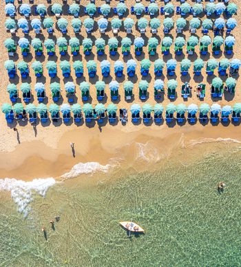 Aerial view of Bat Yam beach with rows of colorful umbrellas on golden sand and people in a small boat on clear water Bat Yam Center District Israel. Aerial view of Bat Yam beach with rows of colorful umbrellas on golden sand and people in a small boat on clear water Bat Yam Center District Israel.