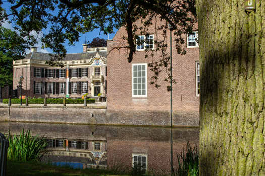 View of Castle Groeneveld with its brick facade and white window frames reflected in the calm water of the moat under a clear blue sky Baarn Utrecht Netherlands.
