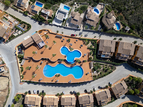 Aerial view of two large uniquely shaped swimming pools surrounded by tiled terraces palm trees and Mediterranean style villas in Moraira Valencian Community Spain.