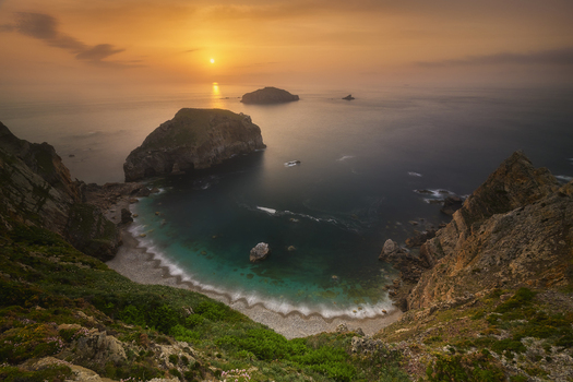View of the rugged coastline with rocky islets and a small cove with turquoise water during a golden sunset Asturias Spain. View of the rugged coastline with rocky islets and a small cove with turquoise water during a golden sunset Asturias Spain.