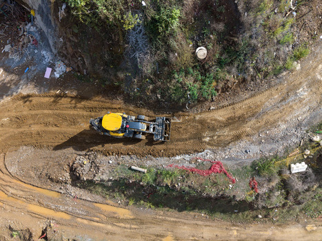 Aerial view of a yellow construction vehicle working on a muddy dirt road surrounded by rocky terrain and vegetation in Istanbul Istanbul Turkiye. Aerial view of a yellow construction vehicle working on a muddy dirt road surrounded by rocky terrain and vegetation in Istanbul Istanbul Turkiye.