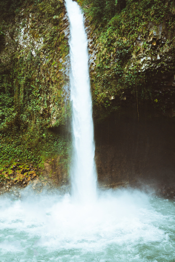 View of a tall waterfall cascading down a lush mossy rock face into a pool of water in Costa Rica.