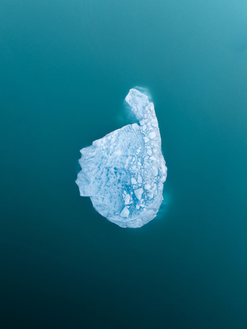 Aerial view of a solitary sculpted iceberg adrift in the glacial lagoon its icy blue form contrasting with the dark placid waters Jokulsarlon Iceland. Aerial view of a solitary sculpted iceberg adrift in the glacial lagoon its icy blue form contrasting with the dark placid waters Jokulsarlon Iceland.