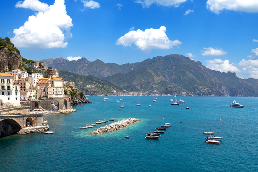Aerial view of Amalfi with historic buildings stone arches and colorful houses along the rugged coastline featuring boats in the turquoise sea in Amalfi Campania Italy. Aerial view of Amalfi with historic buildings stone arches and colorful houses along the rugged coastline featuring boats in the turquoise sea in Amalfi Campania Italy.