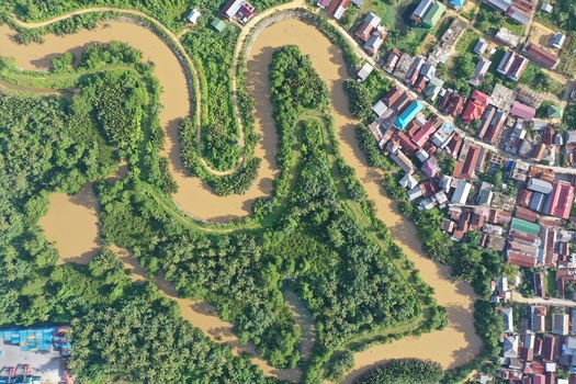 Aerial view of Pulau Maginti featuring a winding river through lush vegetation and a nearby residential area with colorful rooftops in Maginti South East Sulawesi Indonesia.