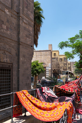 View of the Mosque of al Salih Tala i with vibrant traditional carpets hanging on a railing under a clear blue sky in Cairo Egypt. View of the Mosque of al Salih Tala i with vibrant traditional carpets hanging on a railing under a clear blue sky in Cairo Egypt.