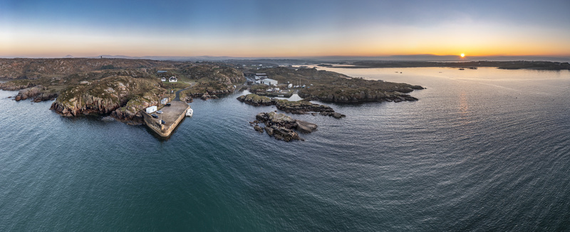Aerial view of the pier and rocky coastline at sunset with calm waters and golden light in Kincasslagh County Donegal Ireland. Aerial view of the pier and rocky coastline at sunset with calm waters and golden light in Kincasslagh County Donegal Ireland.