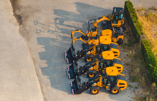 Aerial view of yellow JCB construction machines parked in an industrial yard during golden hour with long shadows on the ground in Le Pouzin Auvergne Rhone Alpes France.