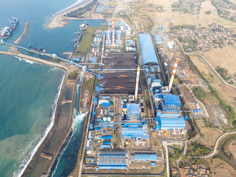 Aerial view of the coal fired power plant with large smokestacks coal storage piles and conveyor belts situated along the coastline in Cilacap Selatan Central Java Indonesia.